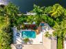 Waterfront property featuring a swimming pool, integrated spa, expansive paver patio, and lush tropical landscaping