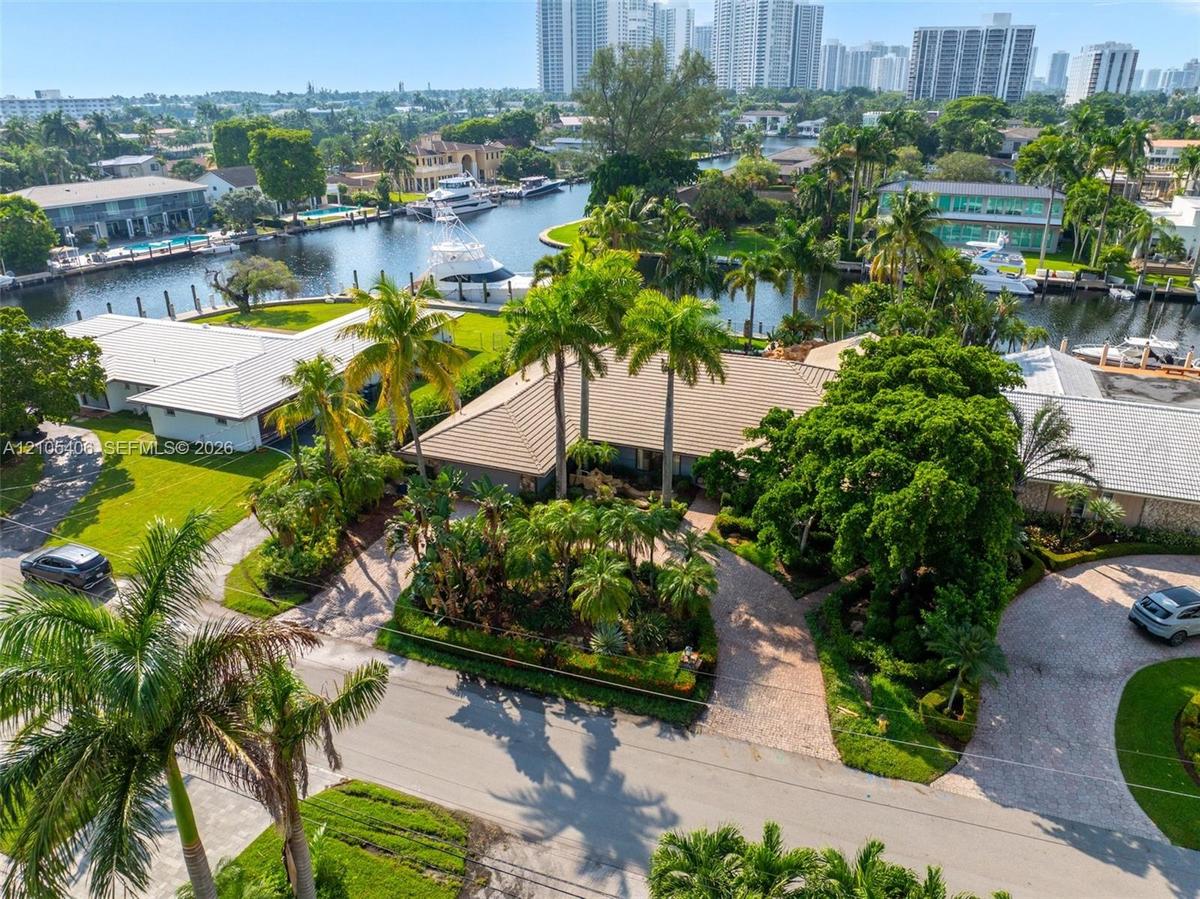 Waterfront property featuring a private dock, lush tropical landscaping, mature palm trees, a circular driveway, and a tiled roof