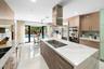 Gourmet kitchen featuring a large central island with integrated cooktop, stainless steel appliances, gloss-finish cabinetry, and a tile backsplash