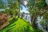 Waterfront property featuring a metal fence, lush artificial turf, mature palm trees, and decorative rock formations