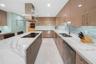Kitchen featuring a large island with an integrated cooktop, white marble-style countertops, glossy tan cabinetry, a stainless steel range hood, and a