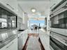Galley kitchen featuring hardwood flooring, white high-gloss cabinetry, integrated stainless steel appliances, and stone countertops