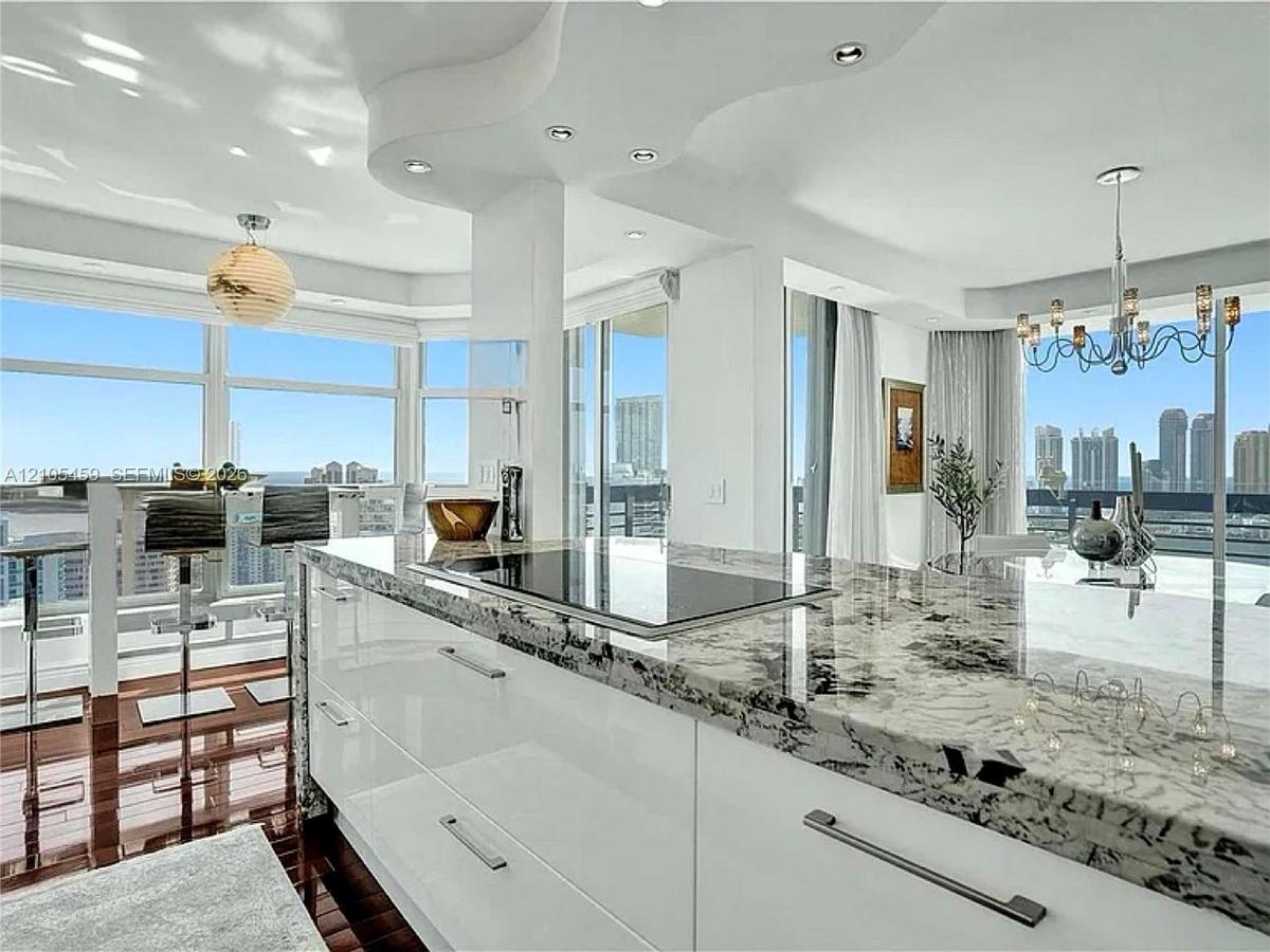 Sleek kitchen island with a built-in cooktop and stone countertop, open concept living area, recessed lighting, expansive floor-to-ceiling windows, an