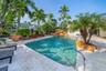 Resort-style pool with rock formation waterfall, surrounded by extensive patio pavers and lush tropical landscaping
