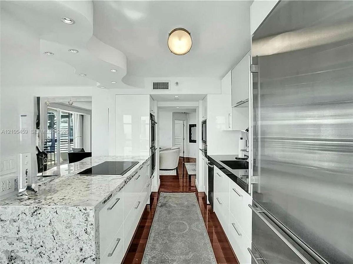 Modern kitchen featuring high-gloss white cabinetry, integrated stainless steel appliances, and wood-finish flooring