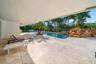 Expansive covered patio featuring light-toned tile flooring, directly accessing a custom pool with a rock waterfall feature and integrated steps