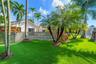 Expansive green lawn with mature palm trees, decorative rock formation, and privacy fencing