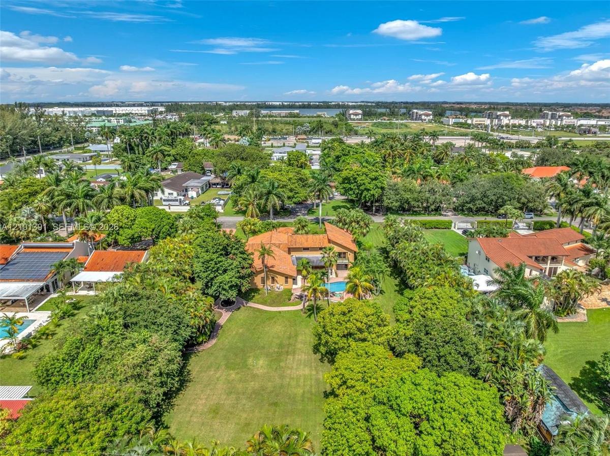 Expansive property with a central residence featuring a barrel tile roof, surrounded by mature trees and lush green landscaping