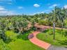 Extensive grounds featuring a circular driveway, mature palm trees, and a terracotta-tiled roof