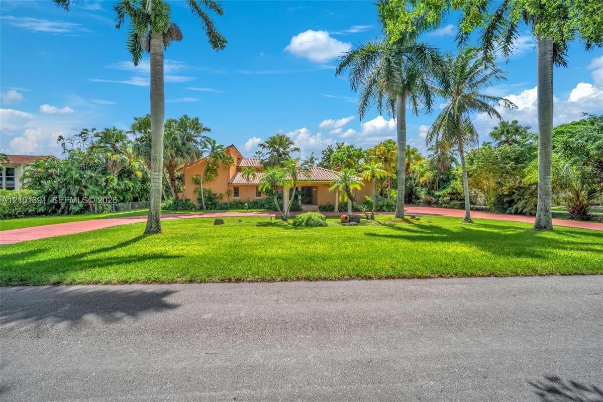 Stucco exterior with a tile roof, surrounded by mature palm trees and lush landscaping