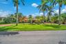 Stucco exterior with a tile roof, surrounded by mature palm trees and lush landscaping