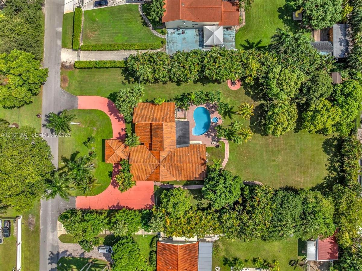 Expansive property featuring a terra cotta roof, a paved circular driveway, a private swimming pool, and a large lawn surrounded by mature trees
