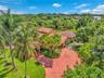 Extensive landscaping with mature palm trees, broad paved driveway, and terracotta roof tiles