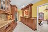 Kitchen featuring extensive wood cabinetry, granite countertops, built-in double ovens, a wine rack, and tile flooring
