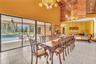 Vaulted wood-paneled ceilings, ornate chandeliers, large format tile flooring, and sliding glass doors opening to a pool deck with a swimming pool