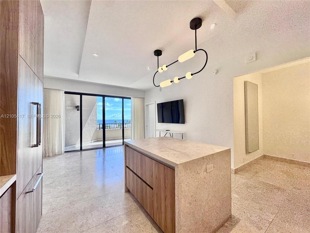 Open-concept living area with large format tile flooring, a kitchen island with a stone finish countertop, built-in wood-finish cabinetry, and a moder