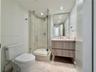 Walk-in shower with glass enclosure, floating wood-finish vanity, stone countertop with integrated sink, rectangular wall-mounted mirror, and tile flo