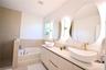 Dual vessel sinks, expansive vanity, built-in bathtub, irregular-shaped mirrors, and gold-tone fixtures