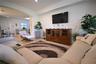 Recessed lighting illuminates the living space, featuring a mounted television and a wood-finish media console with glass-front cabinets