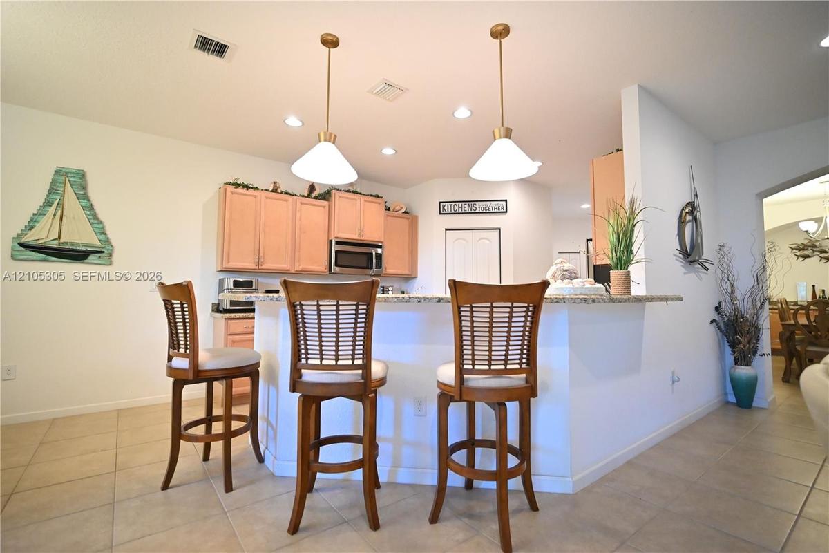 Kitchen with light-toned cabinetry, stainless steel microwave, recessed lighting, and two pendant lights over a countertop bar