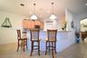 Kitchen with light-toned cabinetry, stainless steel microwave, recessed lighting, and two pendant lights over a countertop bar