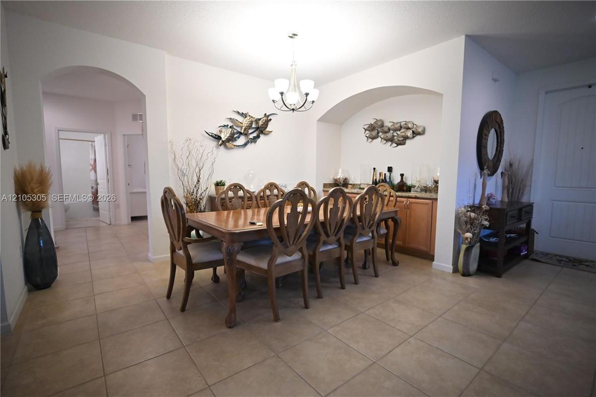 Dining area featuring tile flooring, an arched doorway, and a built-in wet bar with wood-finish cabinetry and a stone countertop
