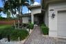 Paver driveway and walkway, arched entryway, exterior wall sconce, and mature landscaping