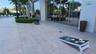 Expansive outdoor patio with large format tile flooring, lush landscaping, and reflective glass exterior