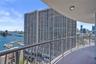Curved balcony with metal railing, waterfront scenery, marina with multiple boats, distant cityscape, and prominent high-rise buildings