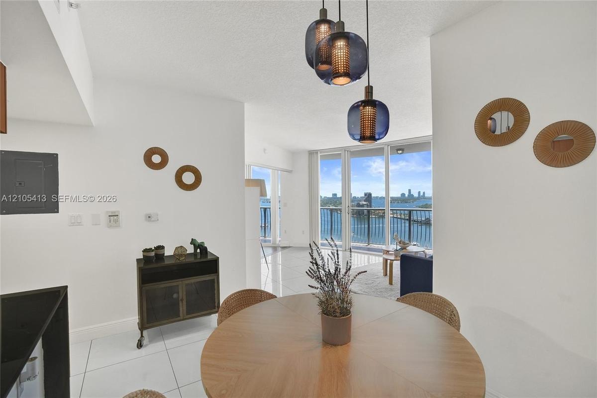 Floor-to-ceiling glass doors with direct water frontage, white tile flooring, and integrated pendant lighting