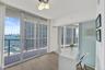 Expansive floor-to-ceiling glass sliding doors, private balcony with metal railings, wood-finish flooring, built-in counter surface, and a frosted gla