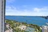 Expansive water frontage, numerous boats on the water, lush green parkland, visible tennis courts, and a distant cityscape
