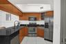 Kitchen featuring wood cabinetry, black countertops, stainless steel appliances, and white tile flooring