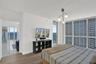 Floor-to-ceiling windows, wood-finish flooring, white walls, modern ceiling light fixture, and a glass-paneled balcony