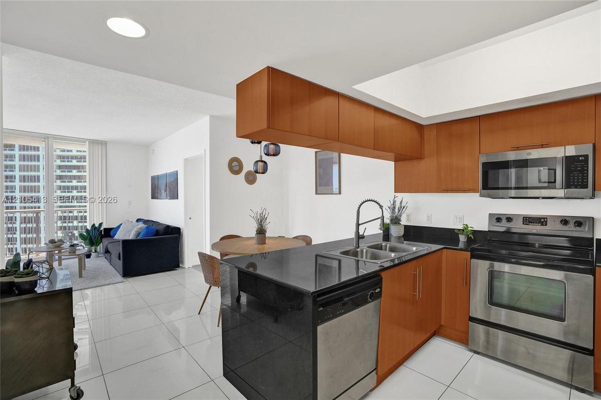 Kitchen featuring wood-finish cabinetry, stainless steel appliances, black countertops, and a stainless steel sink with a gooseneck faucet