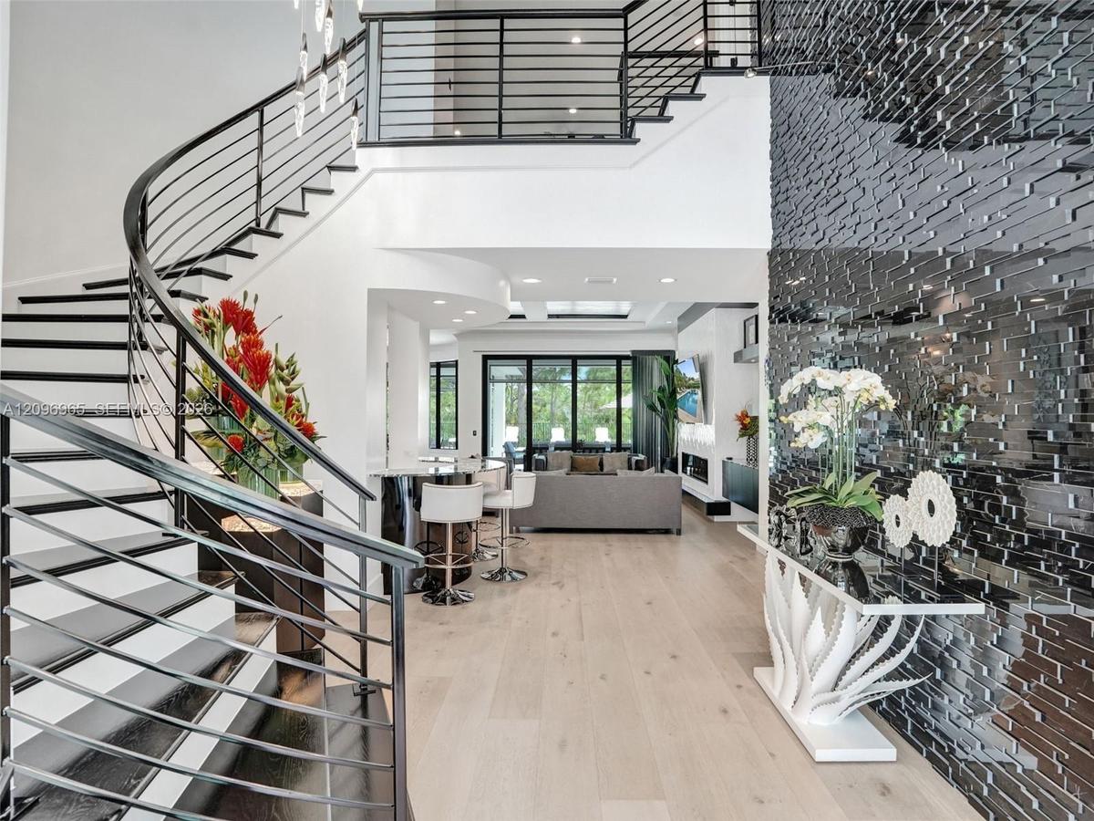 Curved staircase with black metal railings, light wood-finish flooring, and a textured black accent wall