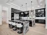 Open-concept kitchen featuring high-gloss cabinetry, a waterfall-edge stone island, wood-finish flooring, a coffered ceiling with a black wood-plank i