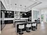 Tray ceiling with dark wood-finish paneling, intricate wrought iron chandelier, recessed lighting, and kitchen island with stone-finish waterfall edge