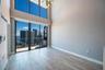Double-height ceiling, floor-to-ceiling windows, sliding glass door to balcony, wood-finish flooring, and modern multi-arm chandelier