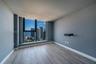 Floor-to-ceiling windows featuring urban and water scenery, wood-finish flooring, and neutral wall color palette
