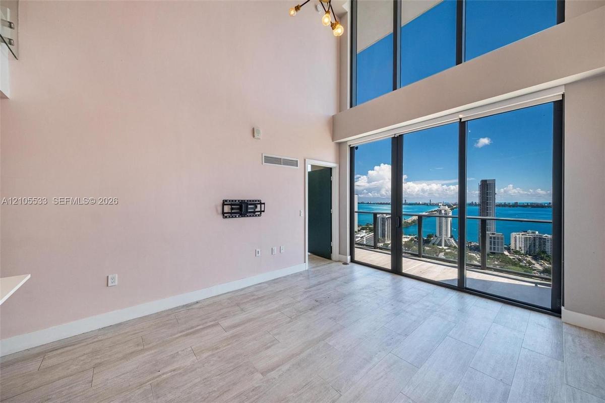 Double-height ceiling, floor-to-ceiling windows, wood-finish tile flooring, and integrated metal balcony railing