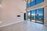 Double-height ceiling, floor-to-ceiling windows, wood-finish tile flooring, and integrated metal balcony railing
