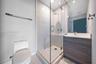 Bathroom featuring a glass-enclosed shower with a rainfall showerhead, a wood-finish vanity with a solid-surface countertop, an integrated sink, and c