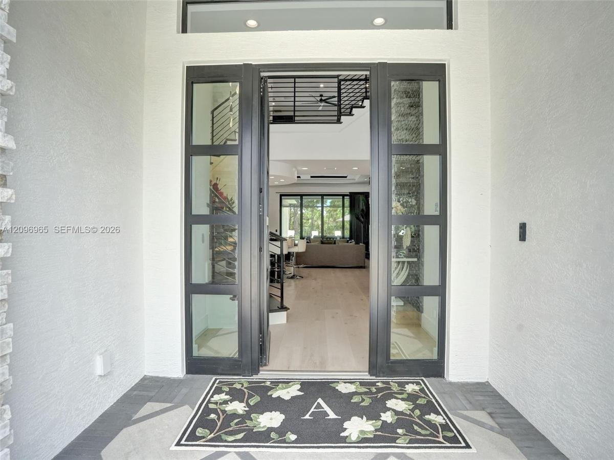 Modern pivot-style entry door featuring a matte black frame with floor-to-ceiling glass paneling and light-toned wood-finish flooring