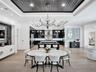 Linear fireplace with textured surround, coffered ceiling featuring dark wood-finish accents, light-tone wood-finish flooring, built-in bar cabinetry,