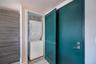 Stacked laundry unit housed in a dedicated closet, featuring a teal louvered door, wood-finish built-in cabinetry, and wood-finish flooring