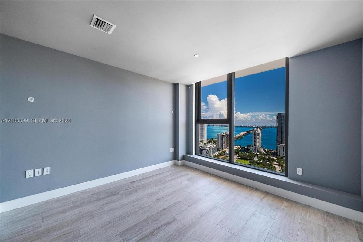 Floor-to-ceiling windows, wood-finish flooring, and expansive water and urban surroundings