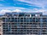High-rise residential exterior featuring expansive floor-to-ceiling windows, wrap-around glass balconies, and a rooftop terrace level