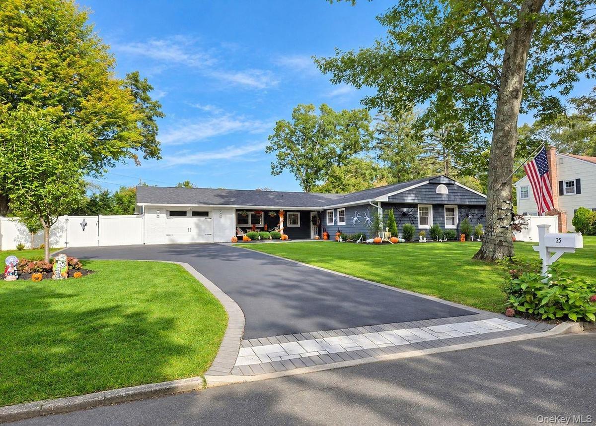 Expansive paved driveway with paver stone accent, white privacy fence, manicured lawn, and mature trees