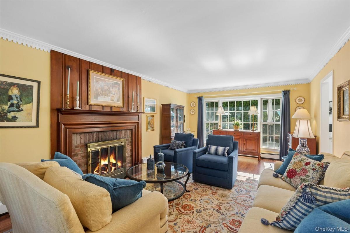 Spacious & sunfilled living room wih fireplace is framed on either end by floor to ceiling windows allowing beautiful views of the gardens